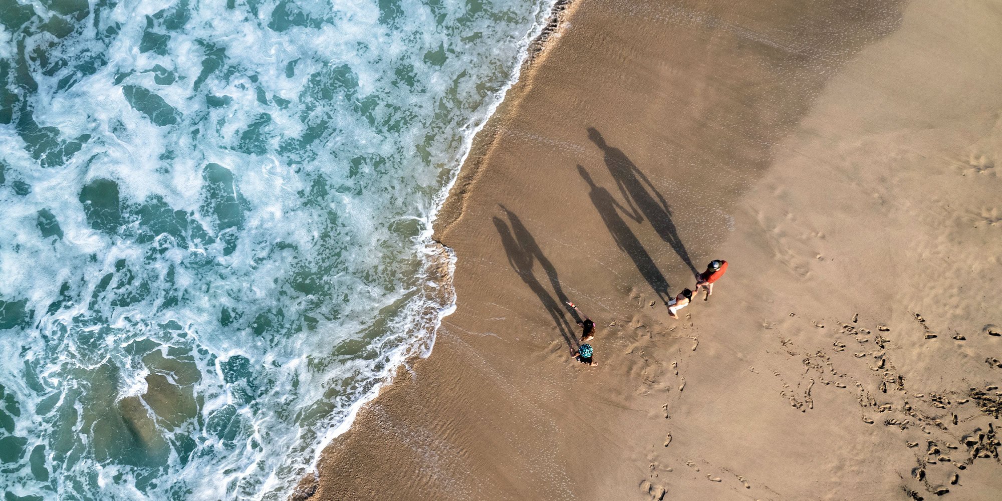 Drone view of a family walking along beach by the ocean