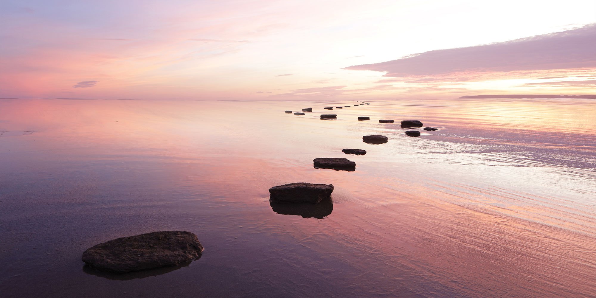 Pink skies and water reflecting over walking stones 